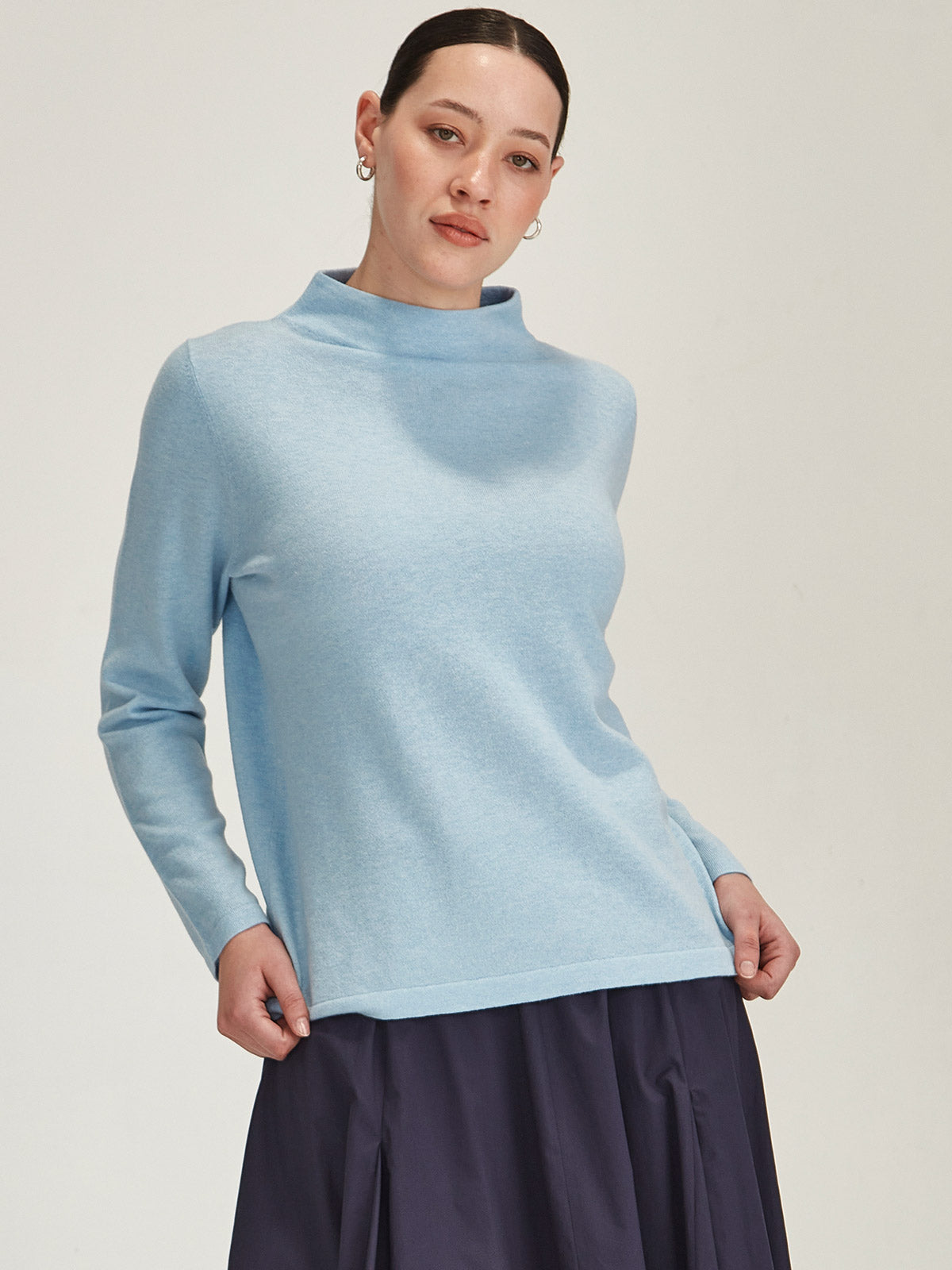 close up of woman wearing sky blue Sills Tasmin funnel neck sweater against grey background