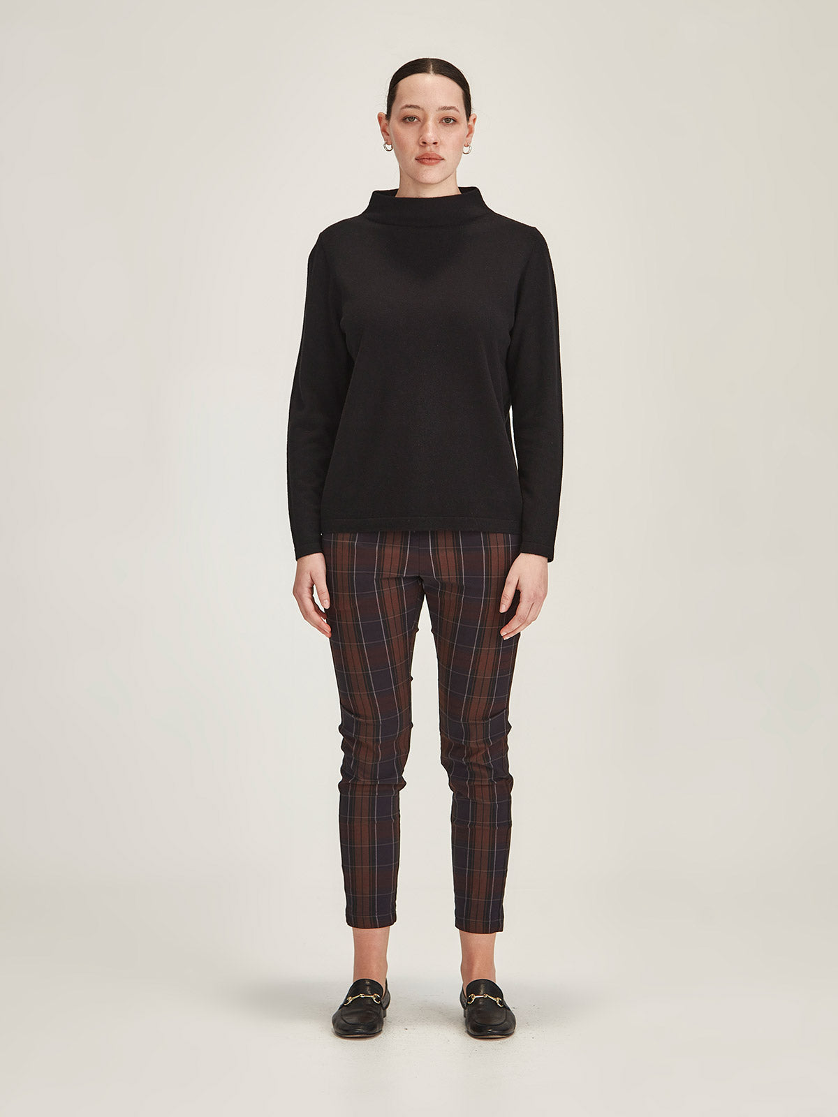 woman wearing black Sills Tasmin funnel neck sweater with plaid Hepburn legging pant against grey background
