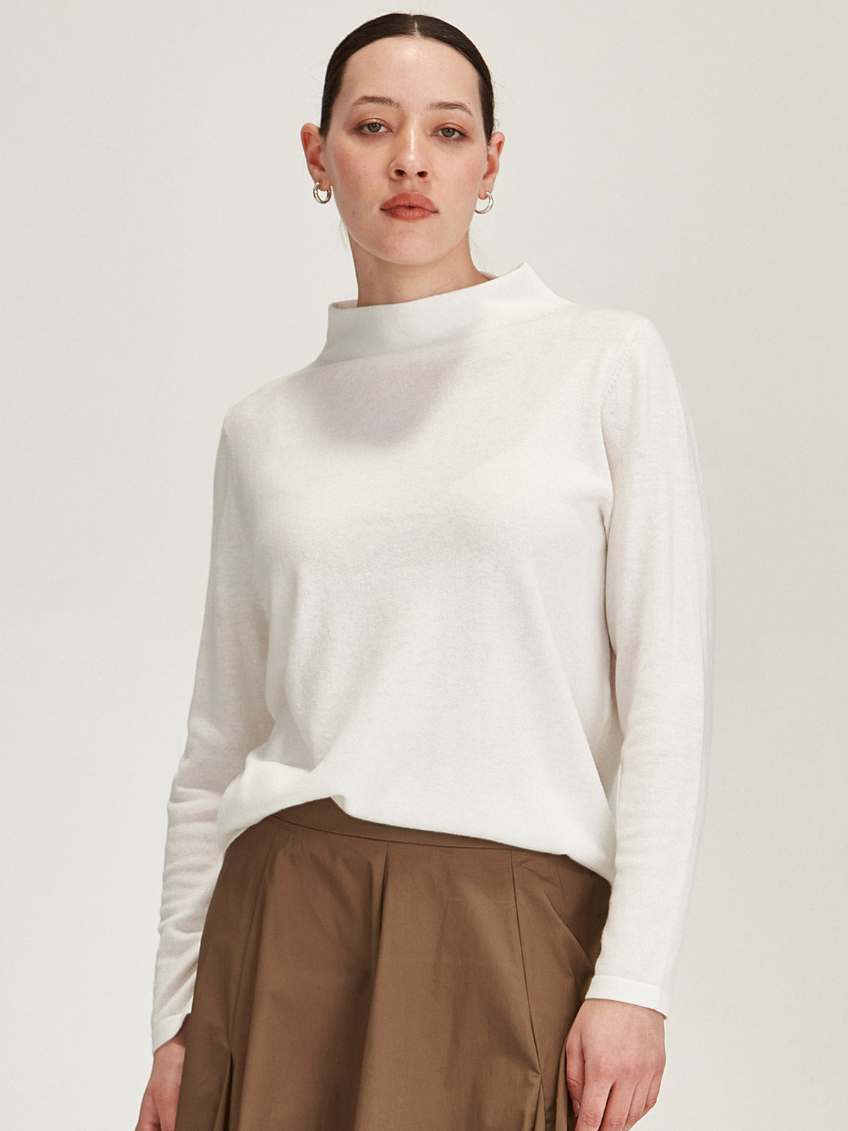 close up of woman wearing off white Sills Tasmin funnel neck sweater against grey background