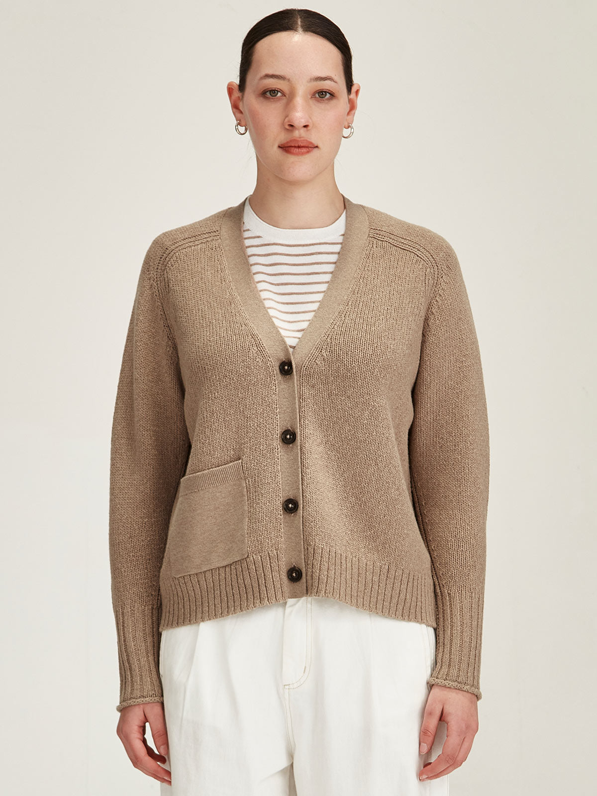close up of woman wearing Sills beige knitted merino/cotton Yuri Cardigan against grey background
