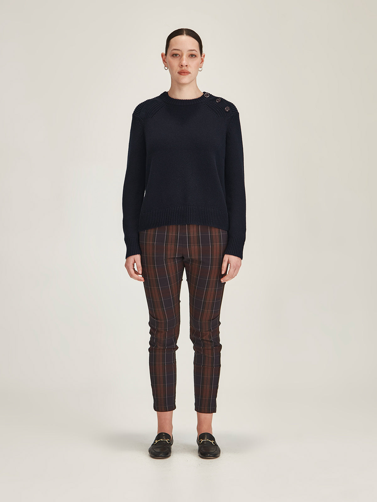 woman wearing Sills camel Colette merino wool/cotton blend sweater with plaid Hepburn pull on pants against grey background