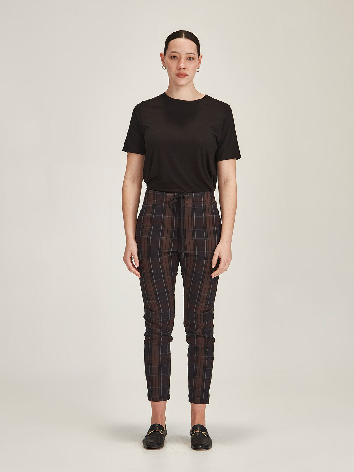 Woman wearing Sills chocolate brown plaid print Emily Joggers and black knit Lena Tee on grey background