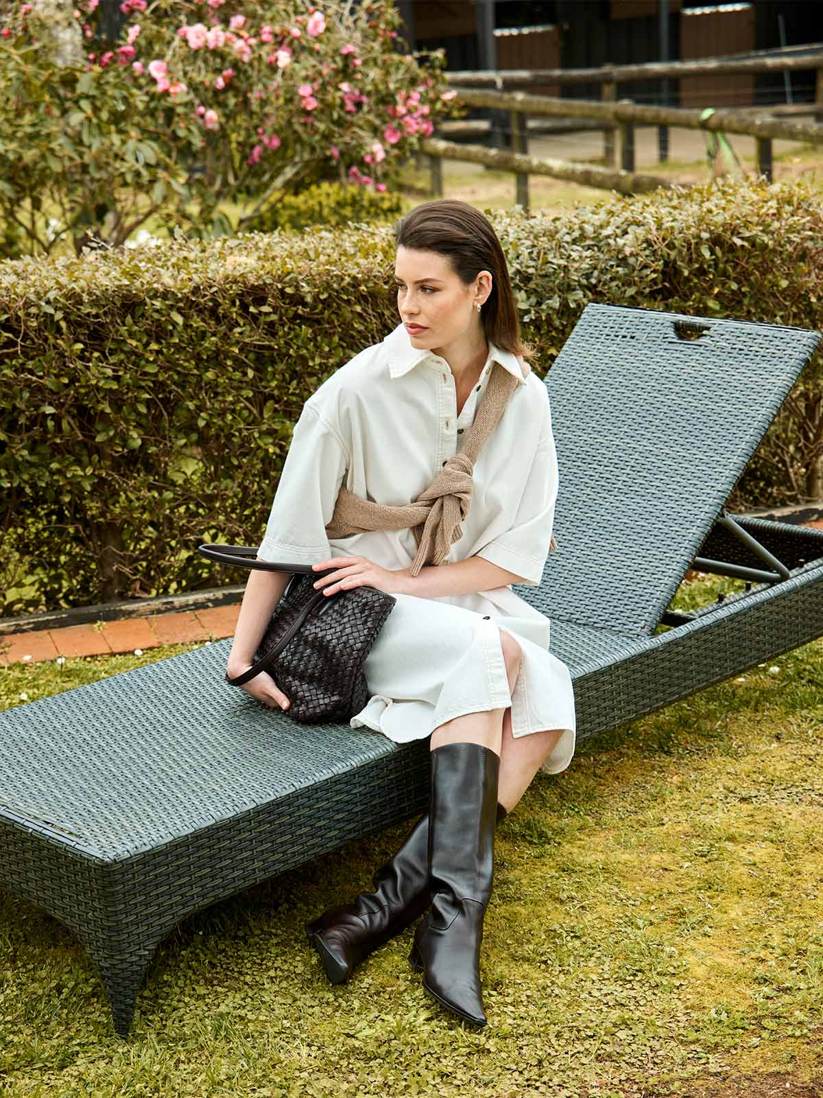 woman sitting outdoors wearing Sills white denim Alexa shirt dress with beige sweater tied at shoulders and Juju & Co bag