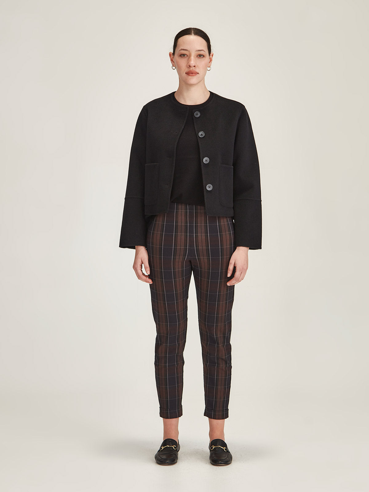 Woman wearing Sills black Emiko wool and cashmere blend jacket with plaid Hepburn pants on grey background