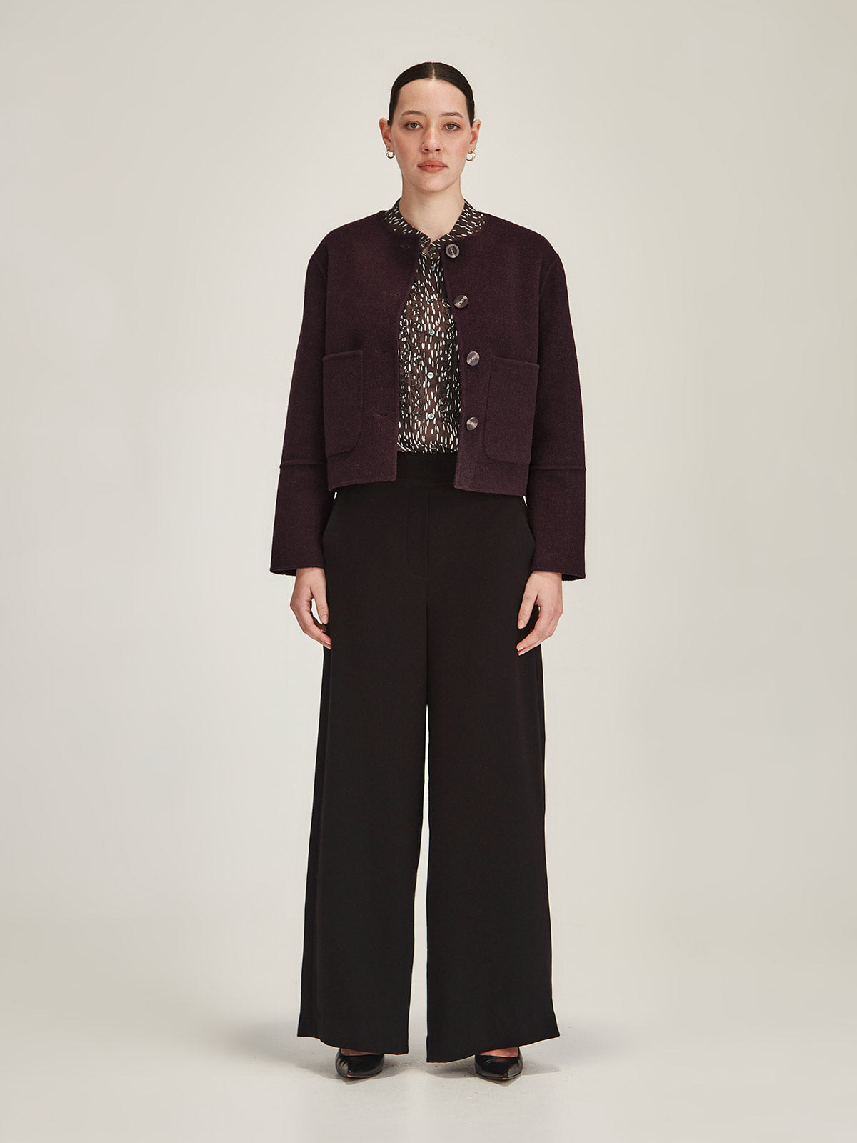 Woman wearing Sills plum Emiko wool and cashmere blend jacket with black Luca Wide Leg Pant on grey background