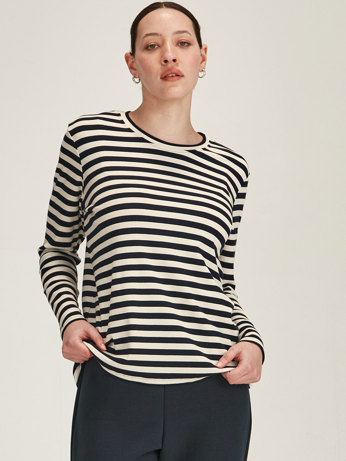 close up of woman in front grey background wearing navy and ivory striped crew neck long sleeve t-shirt