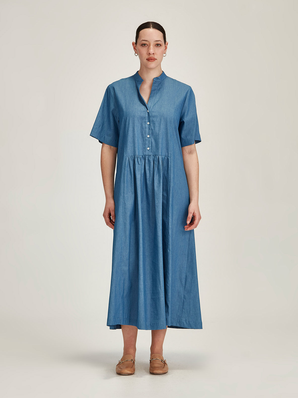 Woman in front of grey background wearing a blue denim Sills Vicky Chambray short sleeve, drop waist midi dress