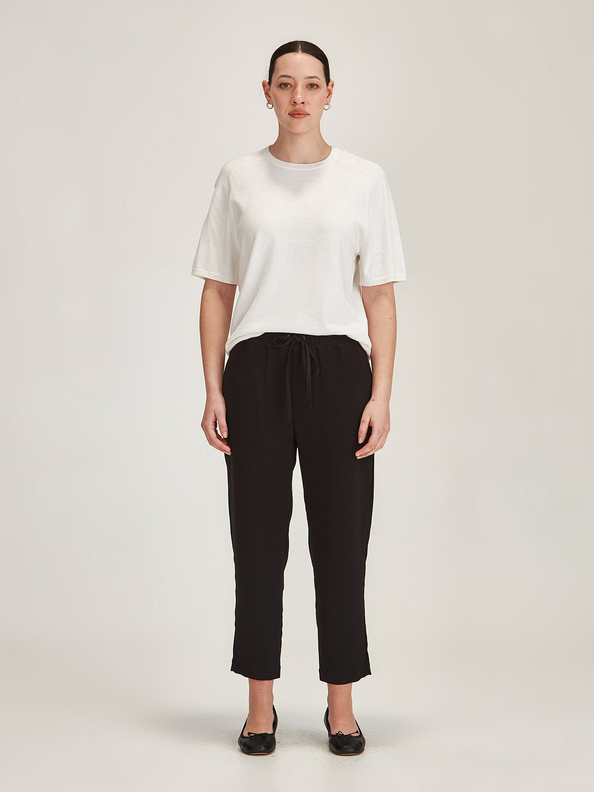 Woman wearing Sills black Joseph crepe Romily Pant with Cecila Knitted T-shirt on grey background