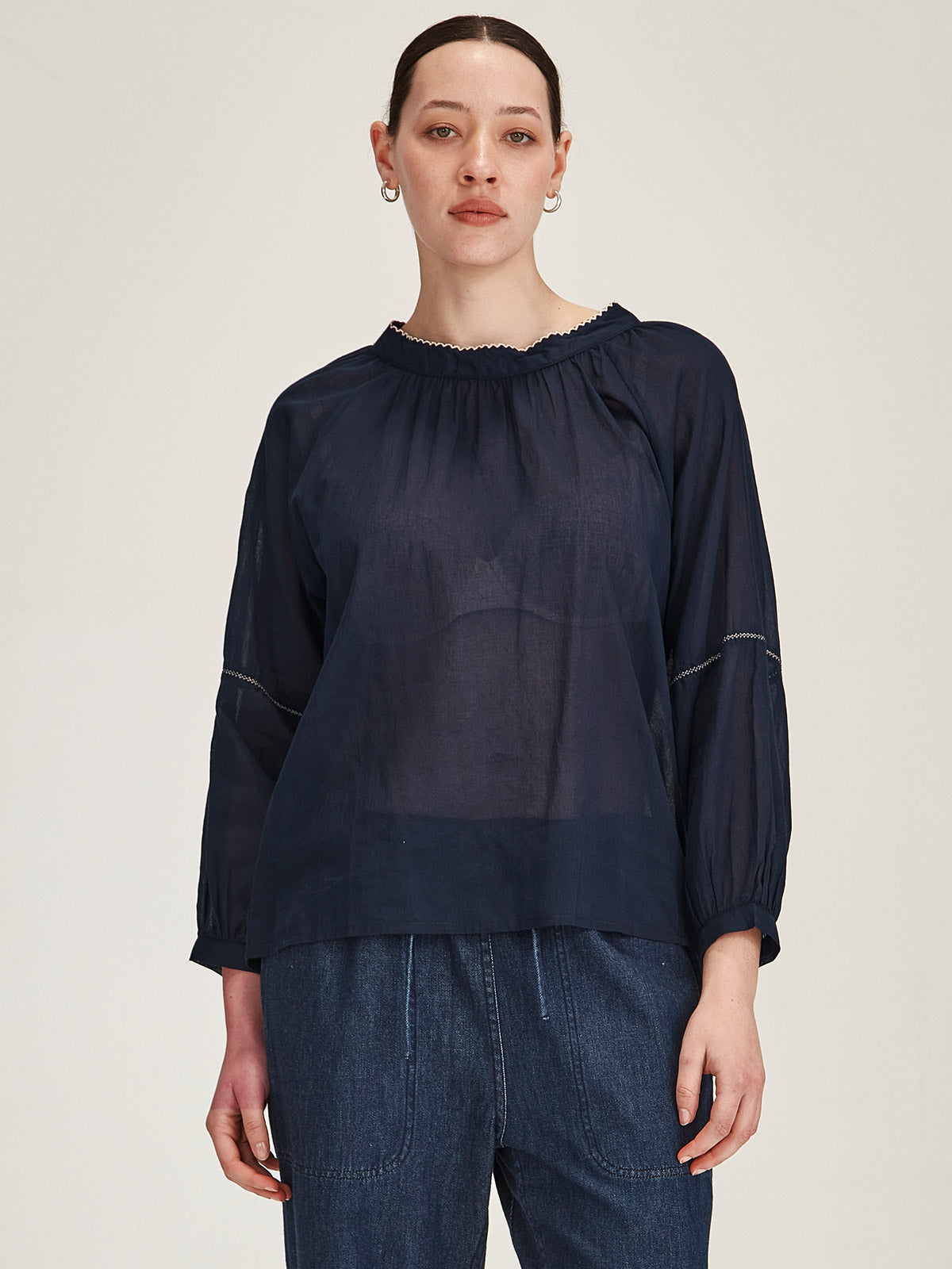 Model wearing a Sills navy organic cotton voile Hana Top with white embroidery against grey background