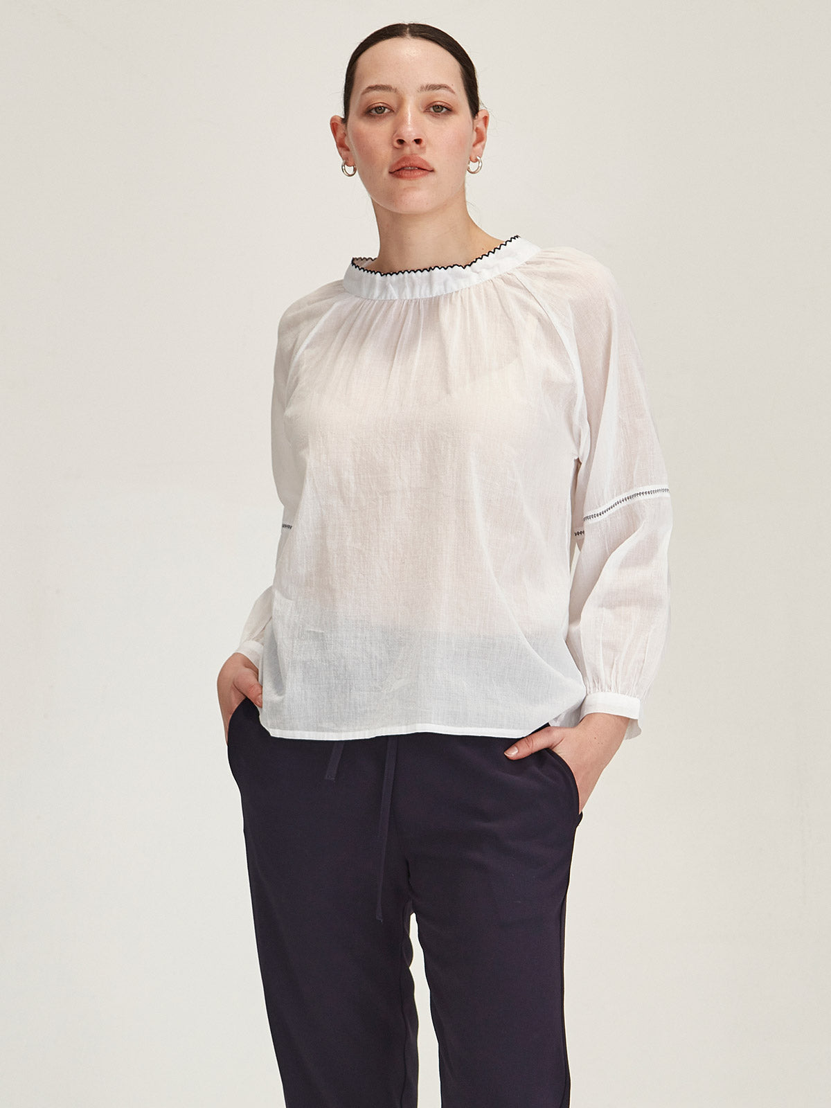 Model wearing a Sills white organic cotton voile Hana Top with navy embroidery against grey background