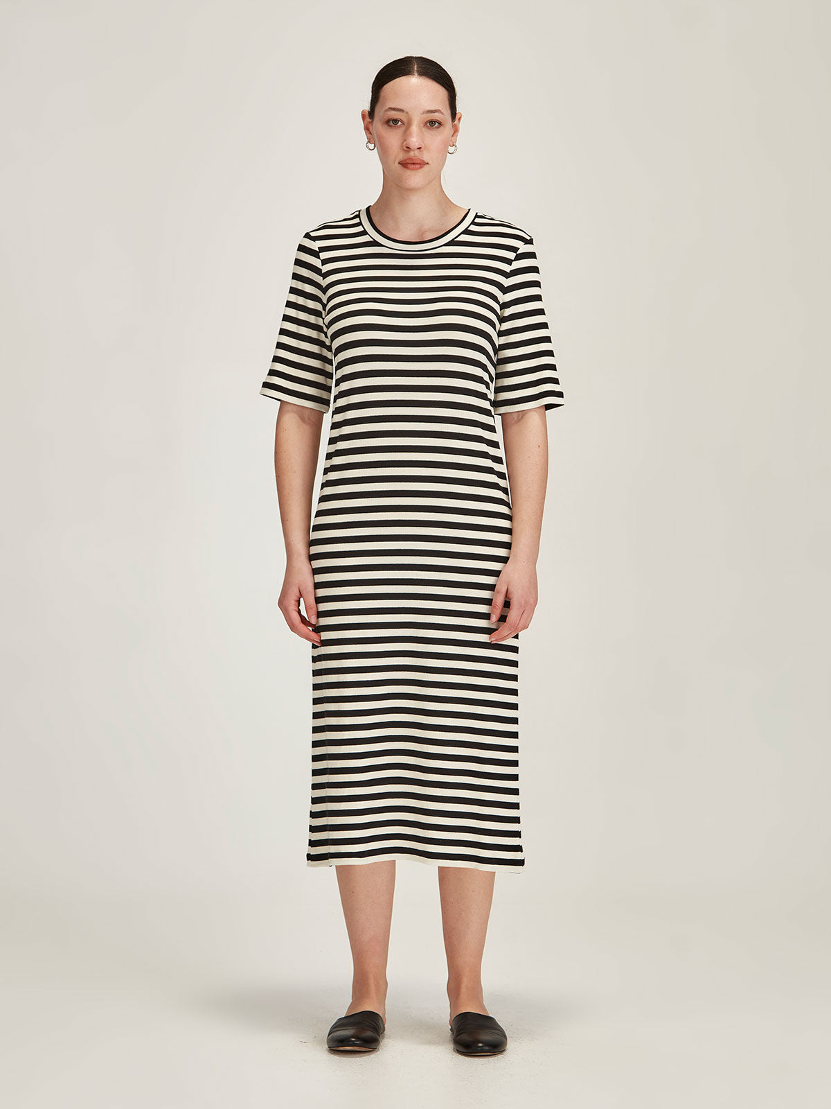 brunette woman wearing black and ivory striped midi t-shirt dress against grey background
