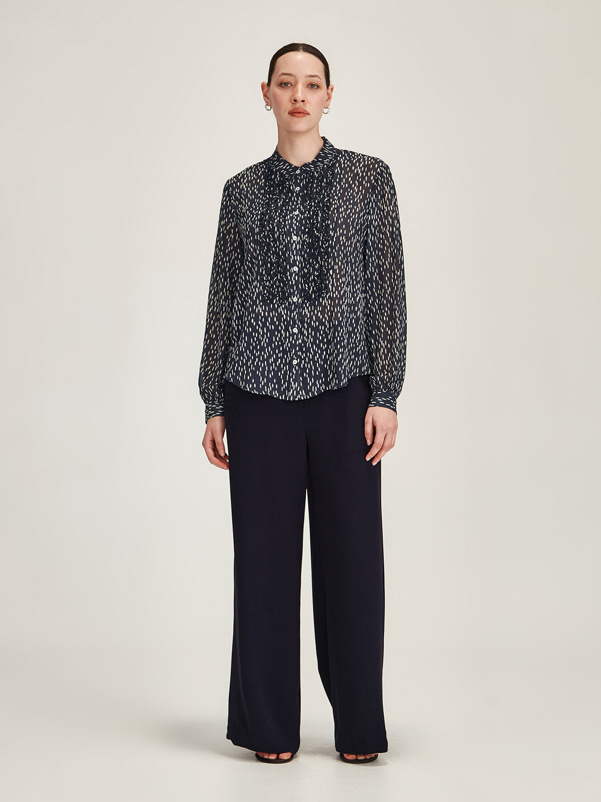 Woman wearing navy Sills Ami Spot polka dot, ruffle detail Shirt with navy Luca Wide Leg crepe Pant against grey background