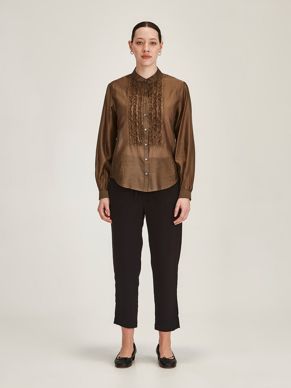 Woman wearing Cinnamon brown Sills Ami Shirt with ruffle detail front with black Romily cropped pant against grey background