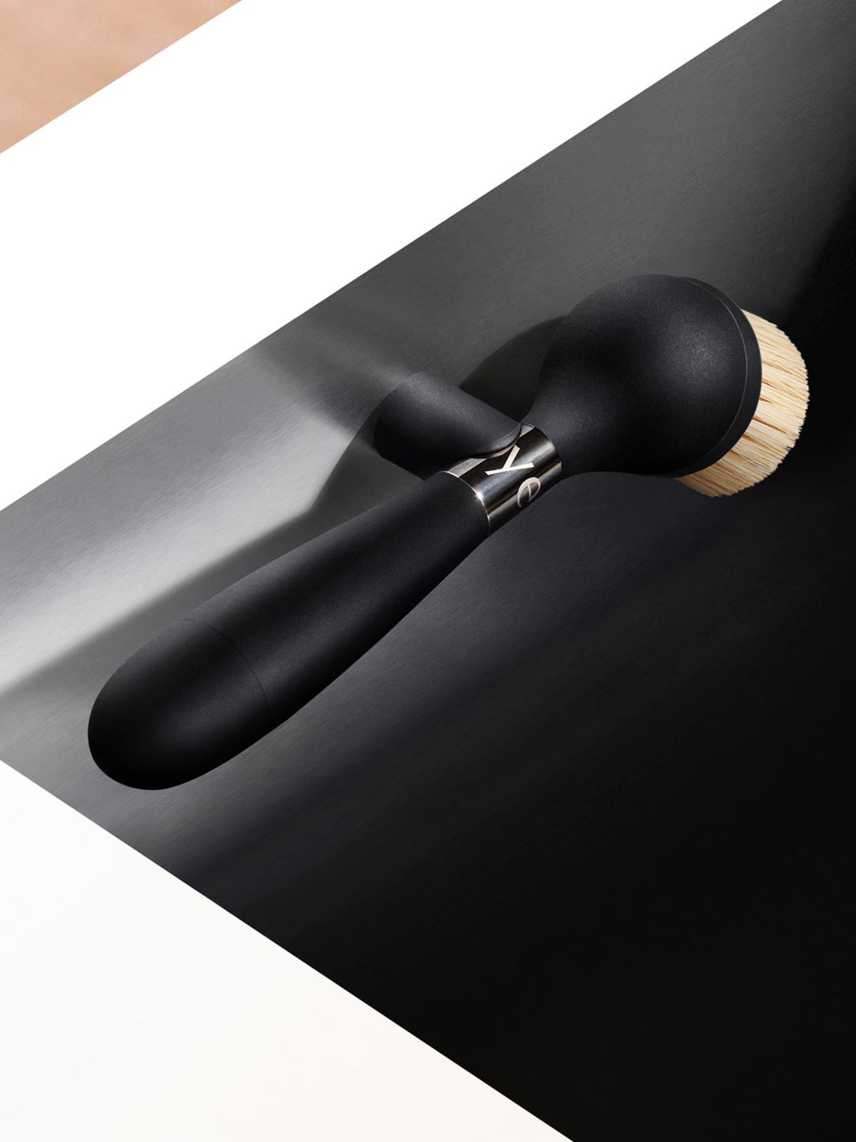 The One Brush V2 Magnetic by Yeseco - Black brush held in hand over a dark undermount sink, showing the magnetic stand and natural sisal fibre brush head.