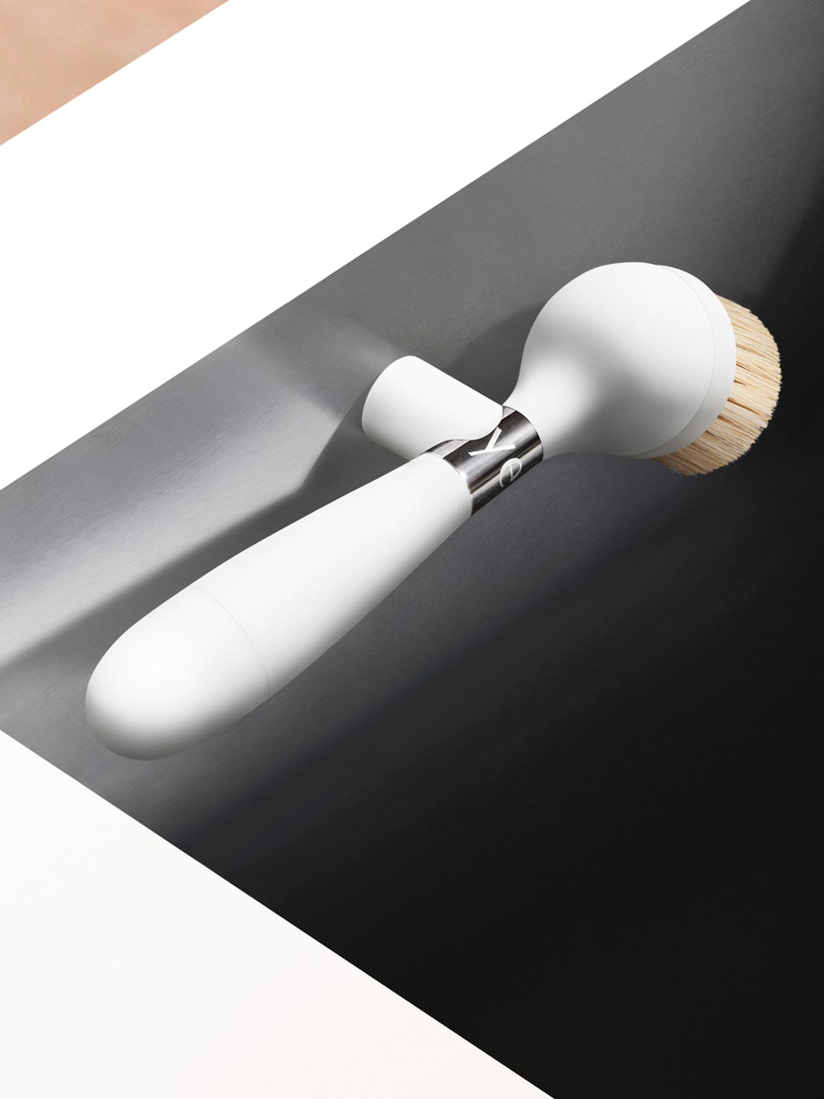 The One Brush V2 Magnetic by Yeseco - White brush held in hand over a dark undermount sink, showing the magnetic stand and natural sisal fibre brush head.