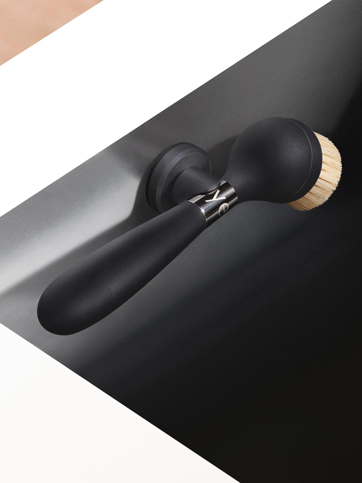 The One Brush V2 Suction by Yeseco - Black version mounted on the edge of a dark undermount sink, showing the suction stand securing the brush in place.