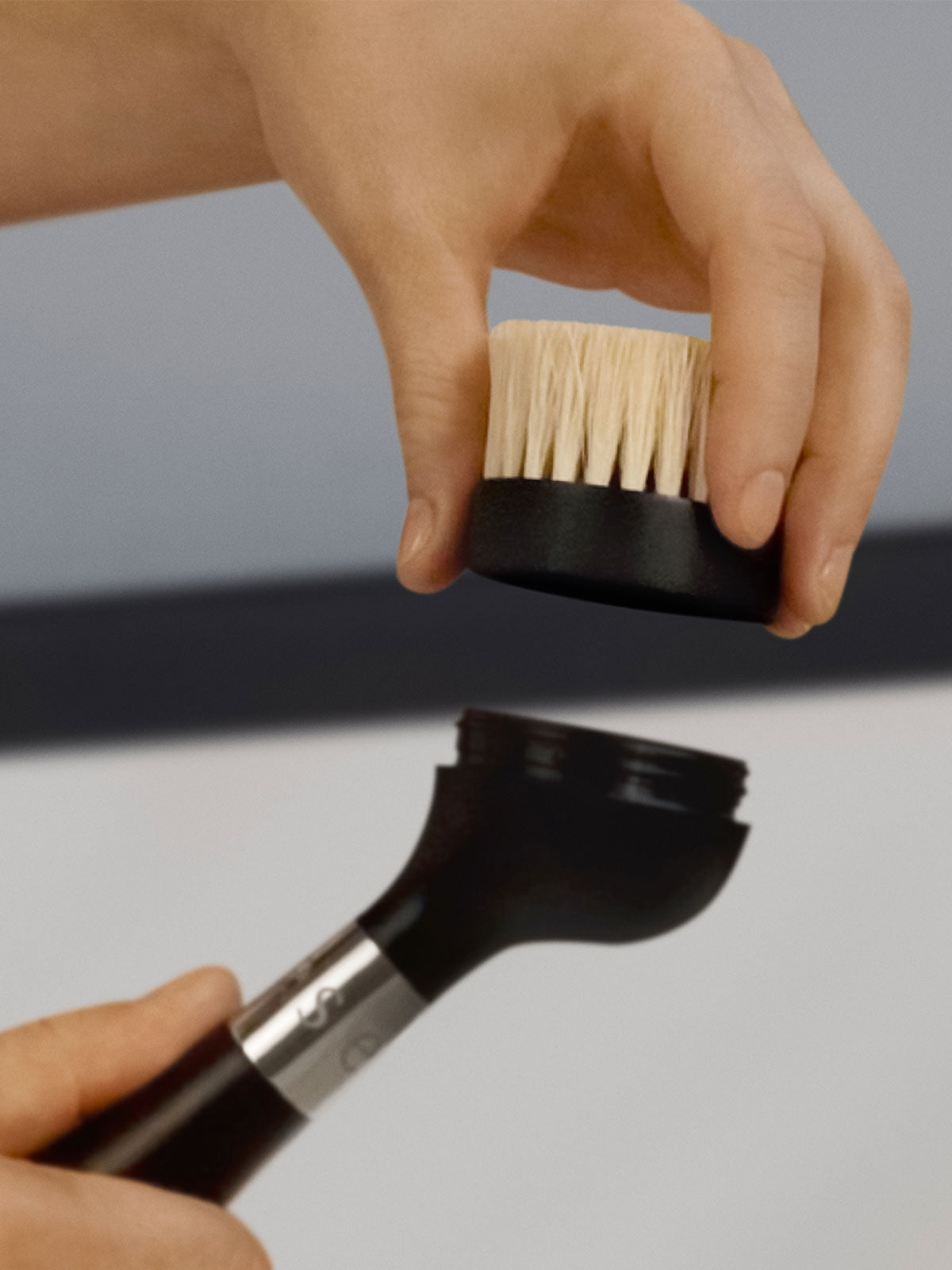 The One Brush V2 Replacement Heads by Yeseco - Hands demonstrating how to detach and replace a black sisal fibre brush head on The One Brush V2 handle, showing the easy twist-off system.